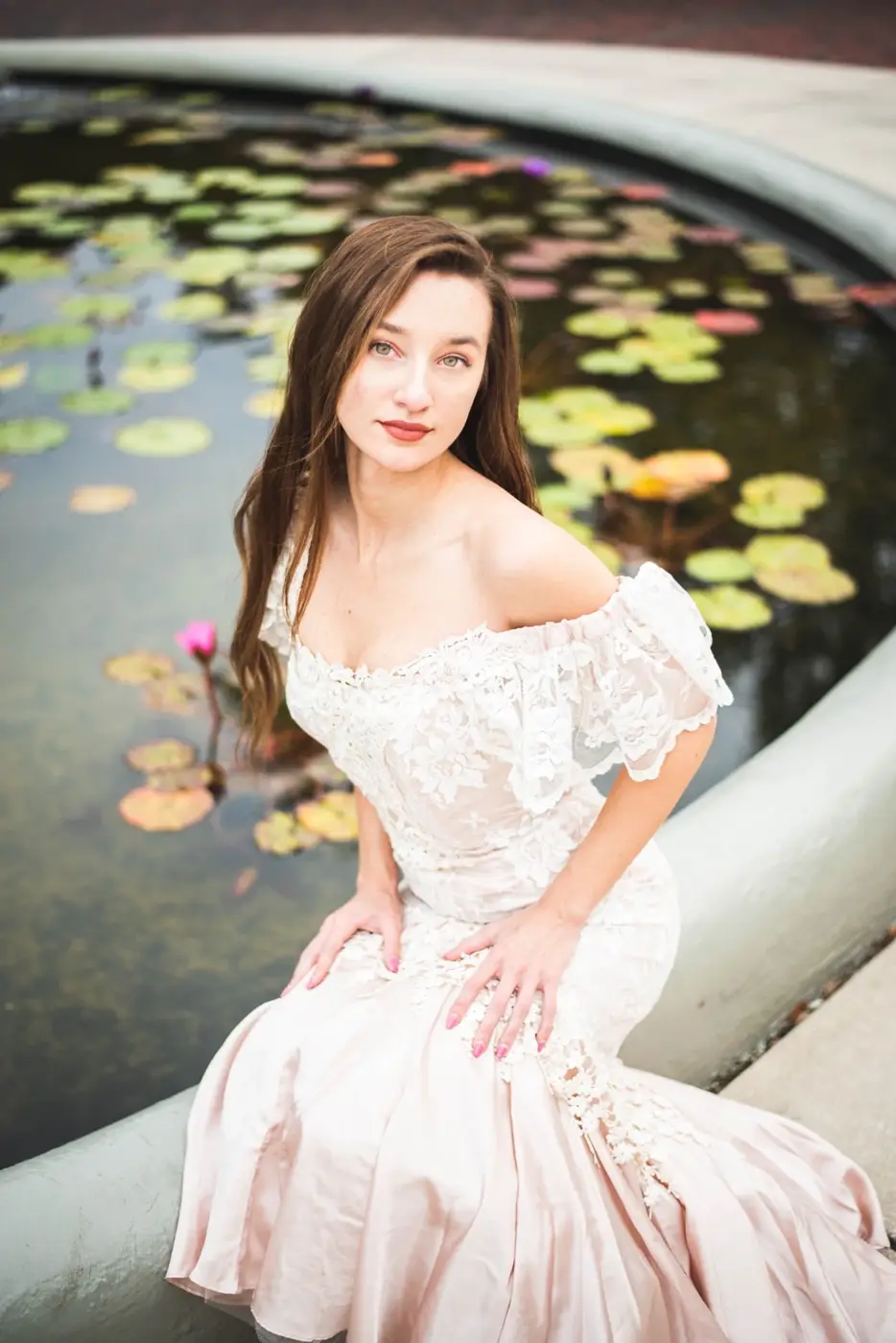 Portrait of a woman in a pale lace dress beside a lily pond