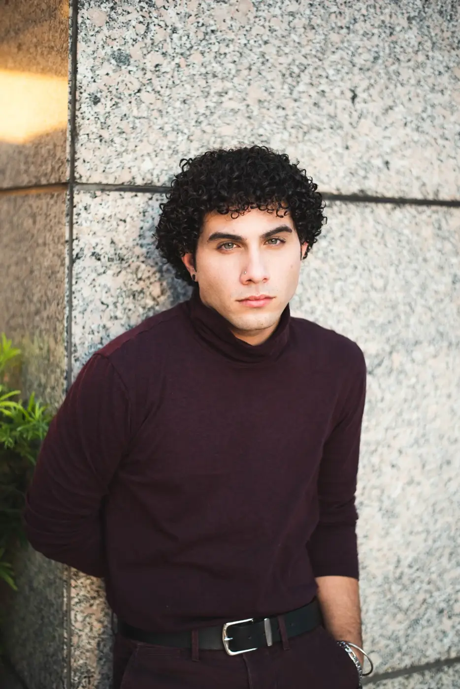 Portrait of a man in a burgundy turtleneck beside a stone wall