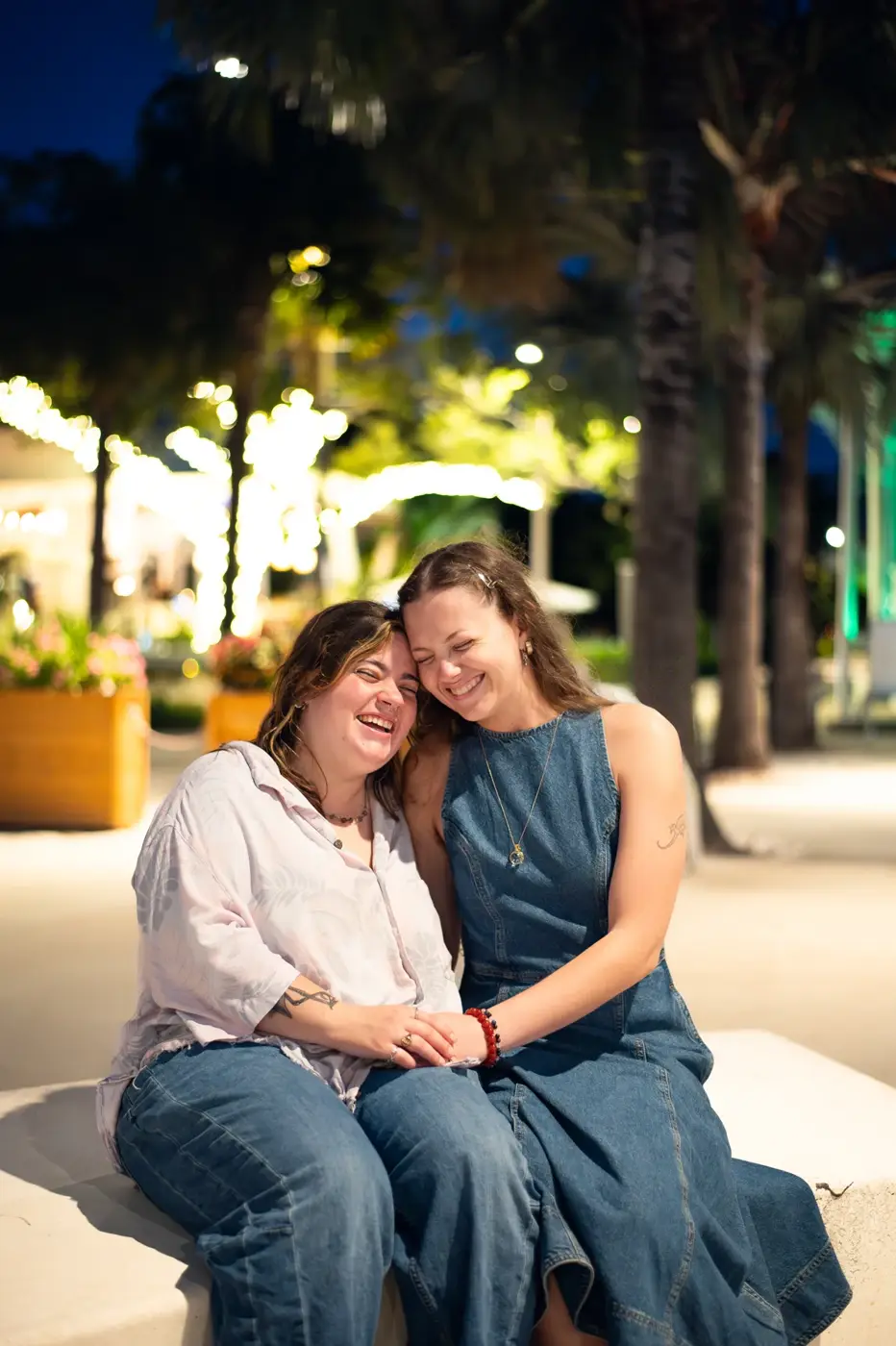 Two women laughing together on a bench beneath evening lights in St. Petersburg, Florida