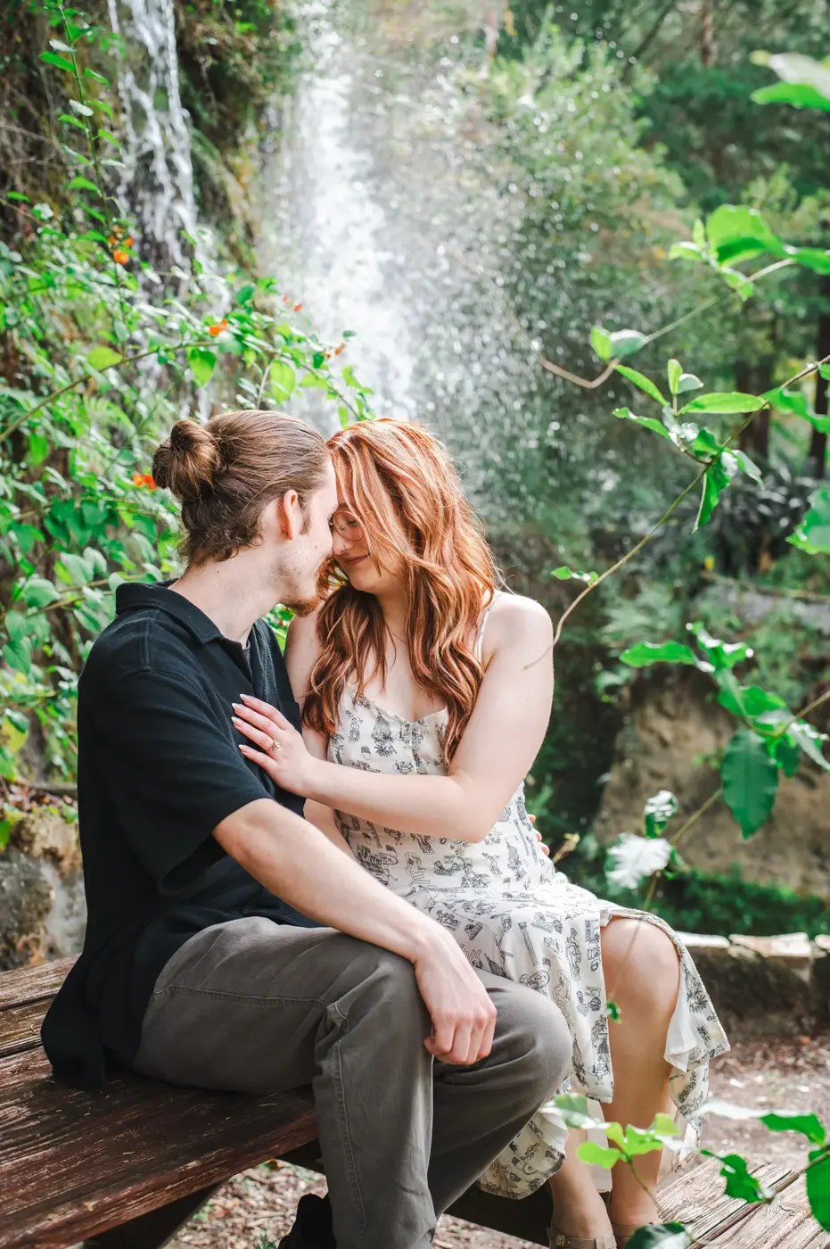 A couple seated together by a waterfall, smiling with their foreheads touching